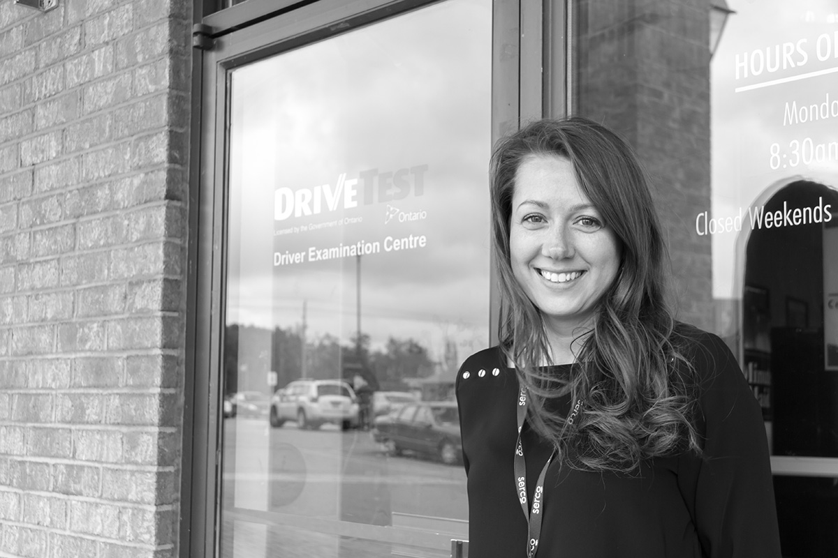 A DriveTest employee standing in front of a Driver Examination Centre.