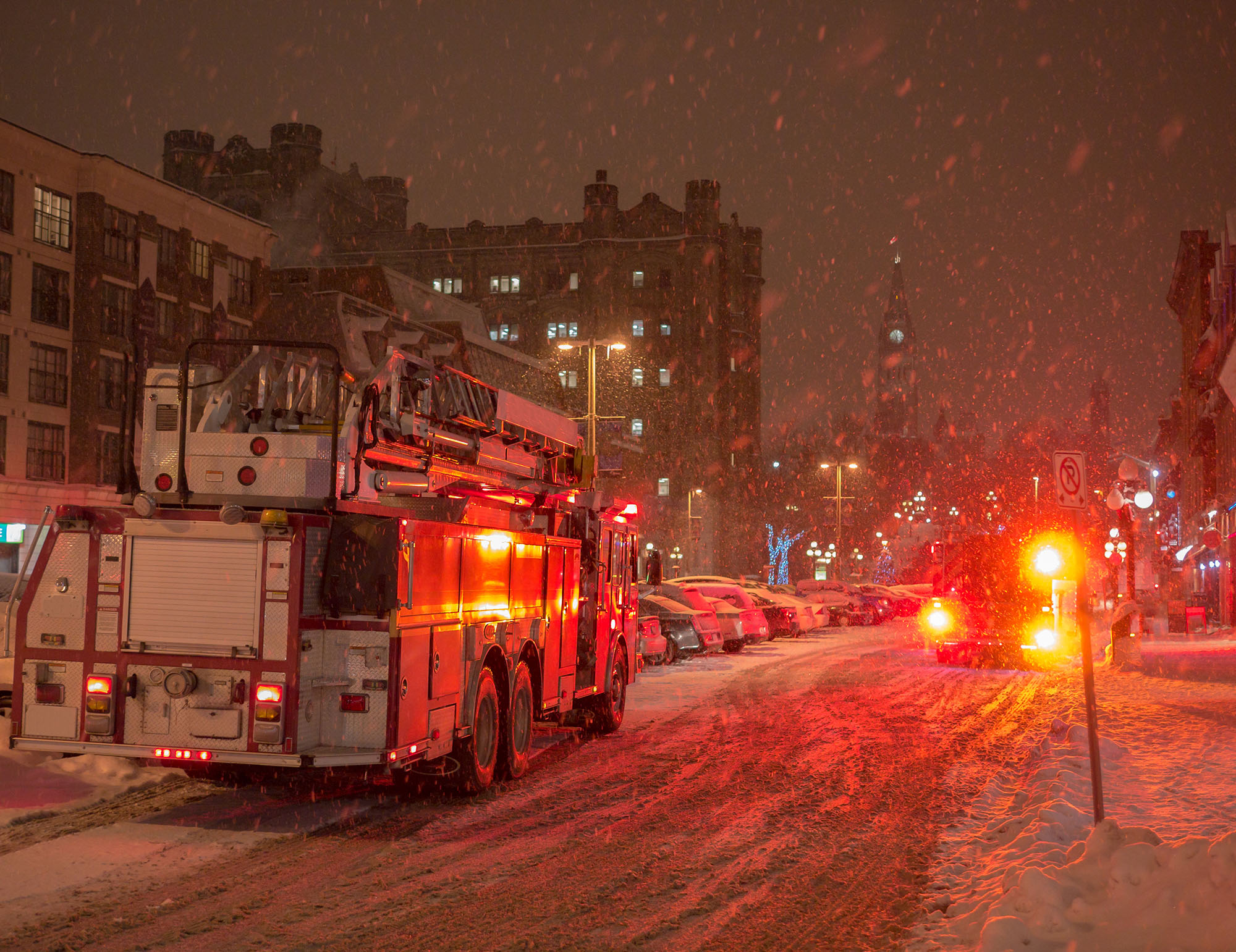 Firetrucks driving down a snowy Ottawa street at night during a snow storm.