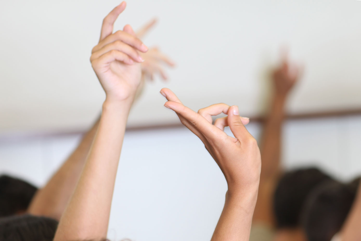 Hands raised in a classroom setting with a blurred background.