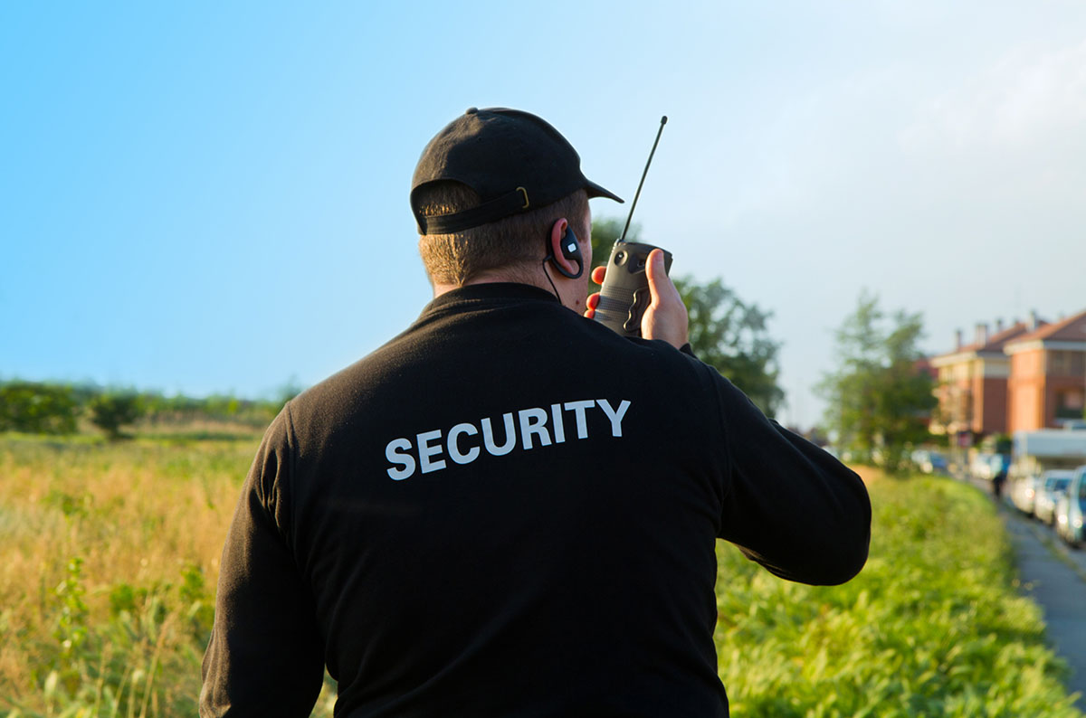 Security guard in a field talking on a portable radio.